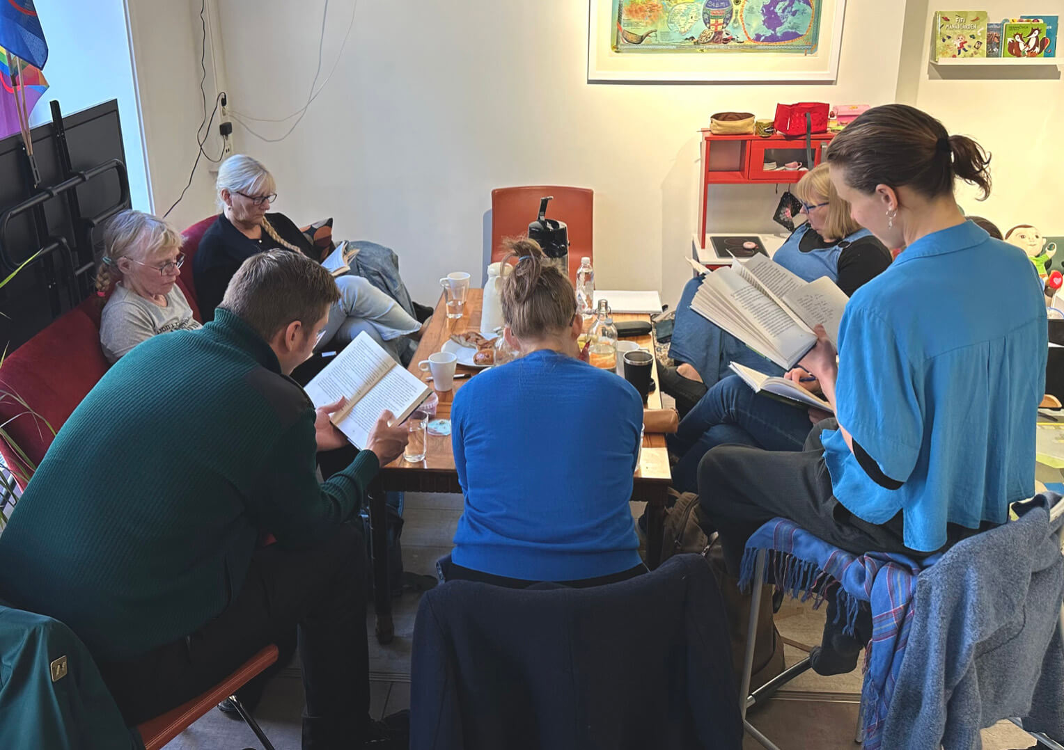 En gruppe personer som sitter rundt et bord og leser i hver sine bøker.