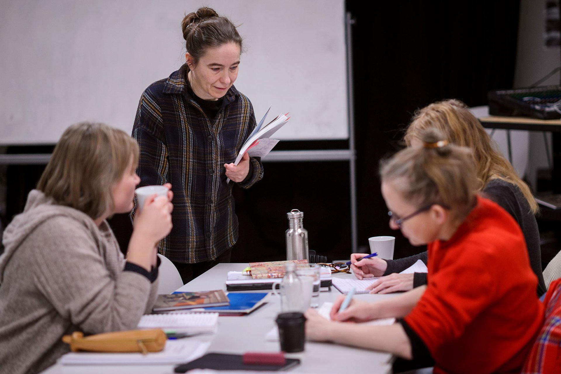Kvinnelig kursleder stående ved arbeidsbord med tre kvinnelige elever rundt.