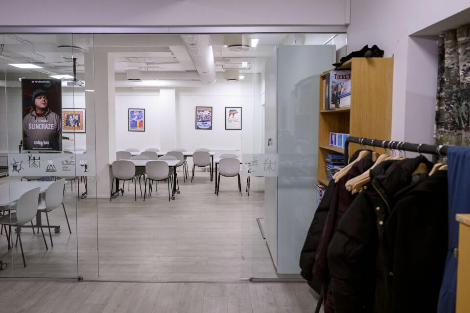 Lyst rom med bord og stoler - klasserom eller møterom. Stativ med kleshengere for jakker.