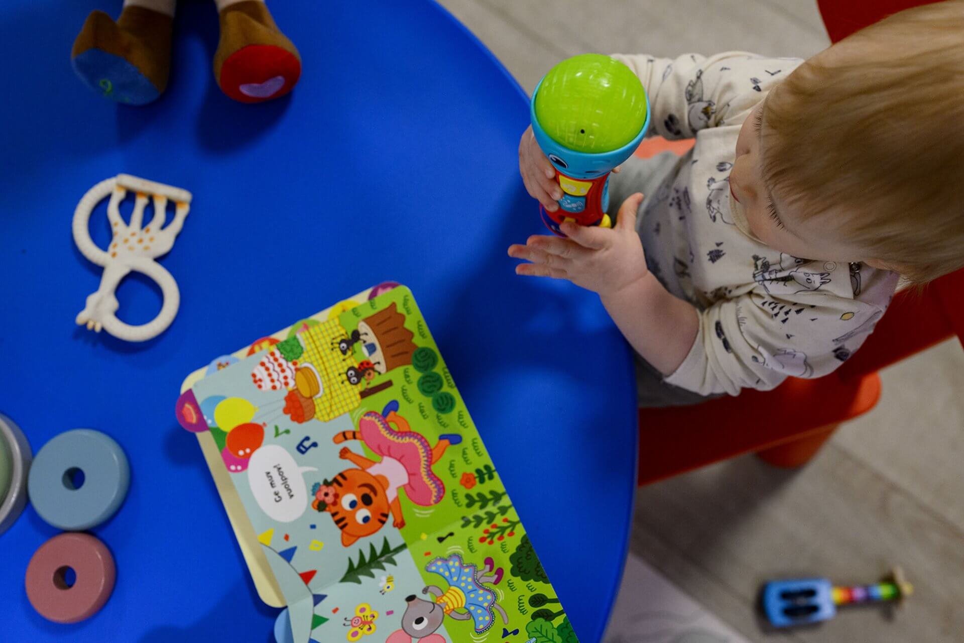 Lite barn som sitter ved et bord med leker og en bok.