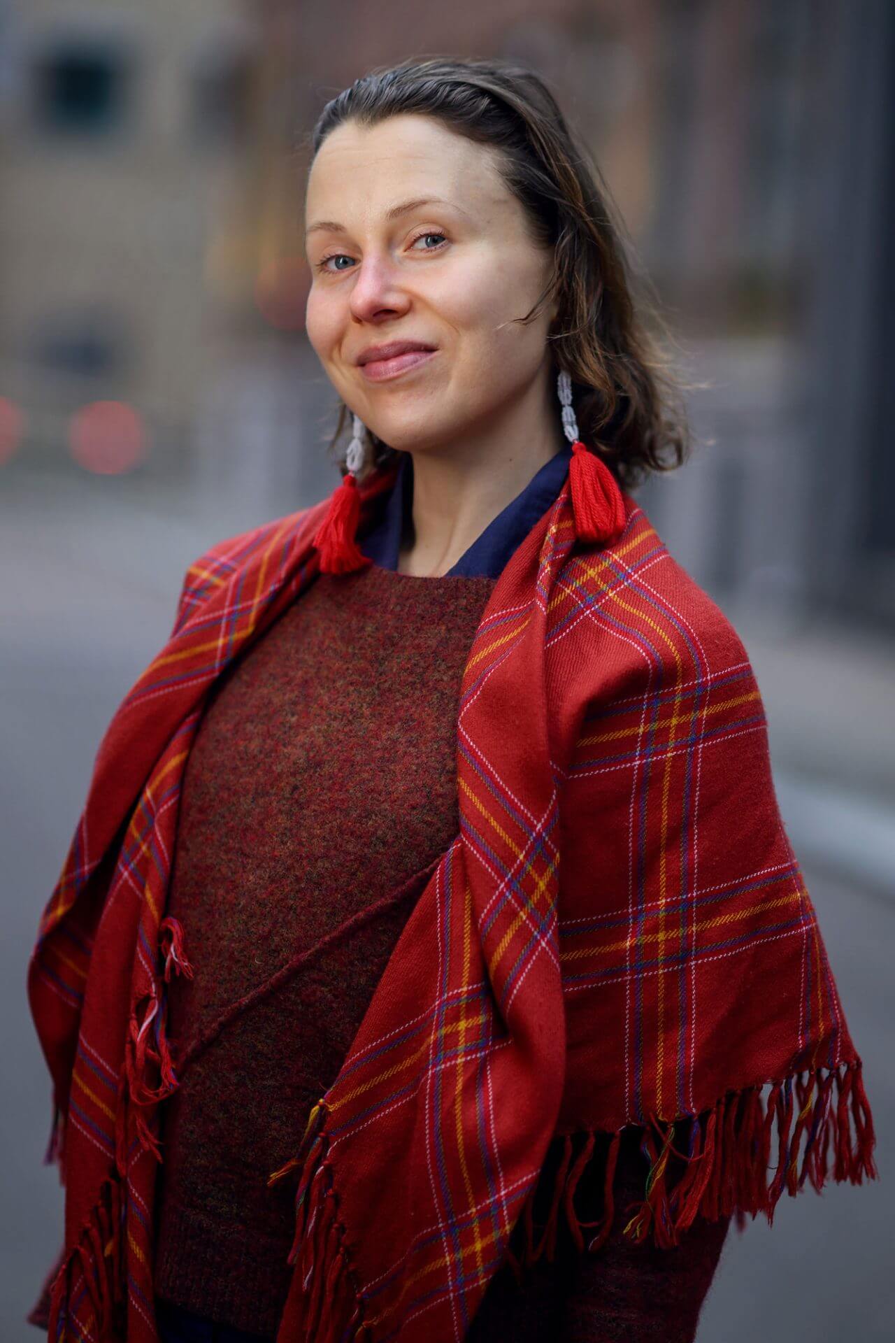 Kvinne med halvlangt mellomblondt hår, og rødrutete samisk sjal rundt skuldrene.