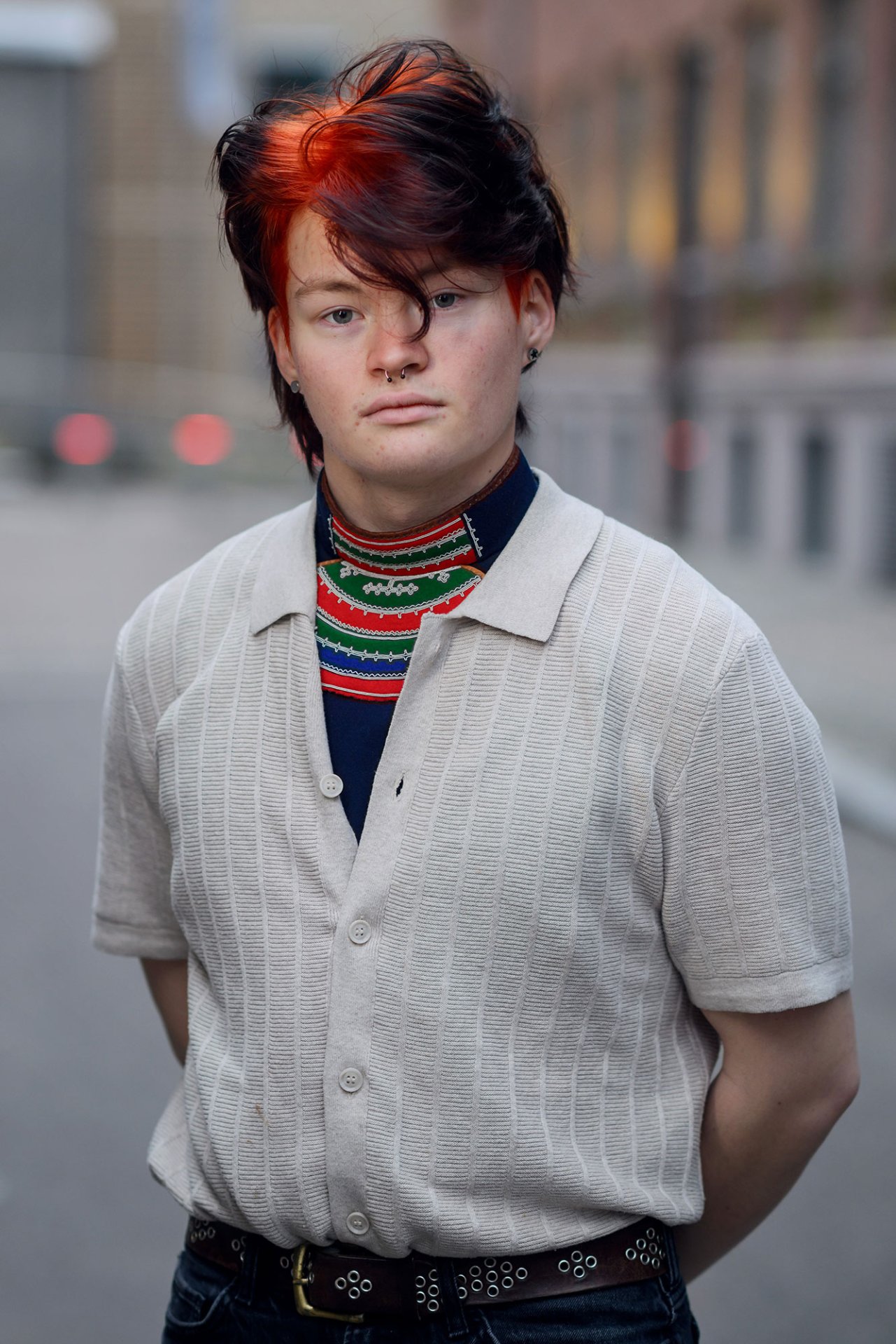 Ung mann med sort og rødt hår, og beige, strikket piquet-skjorte med samisk drakt under.