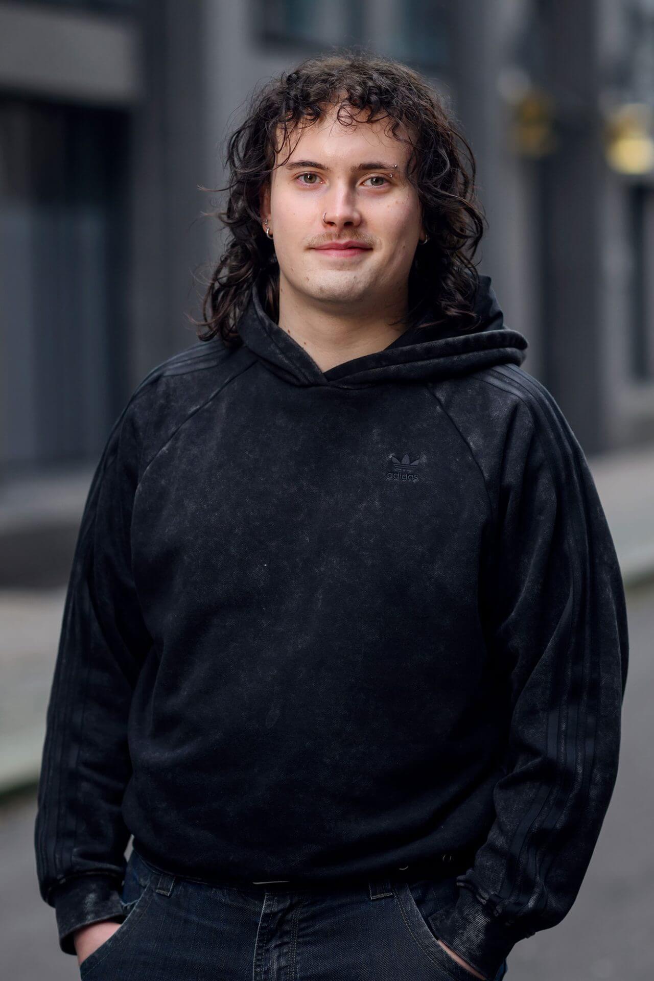 Ung mann med langt, mørkt krøllete hår og sort hettegender.