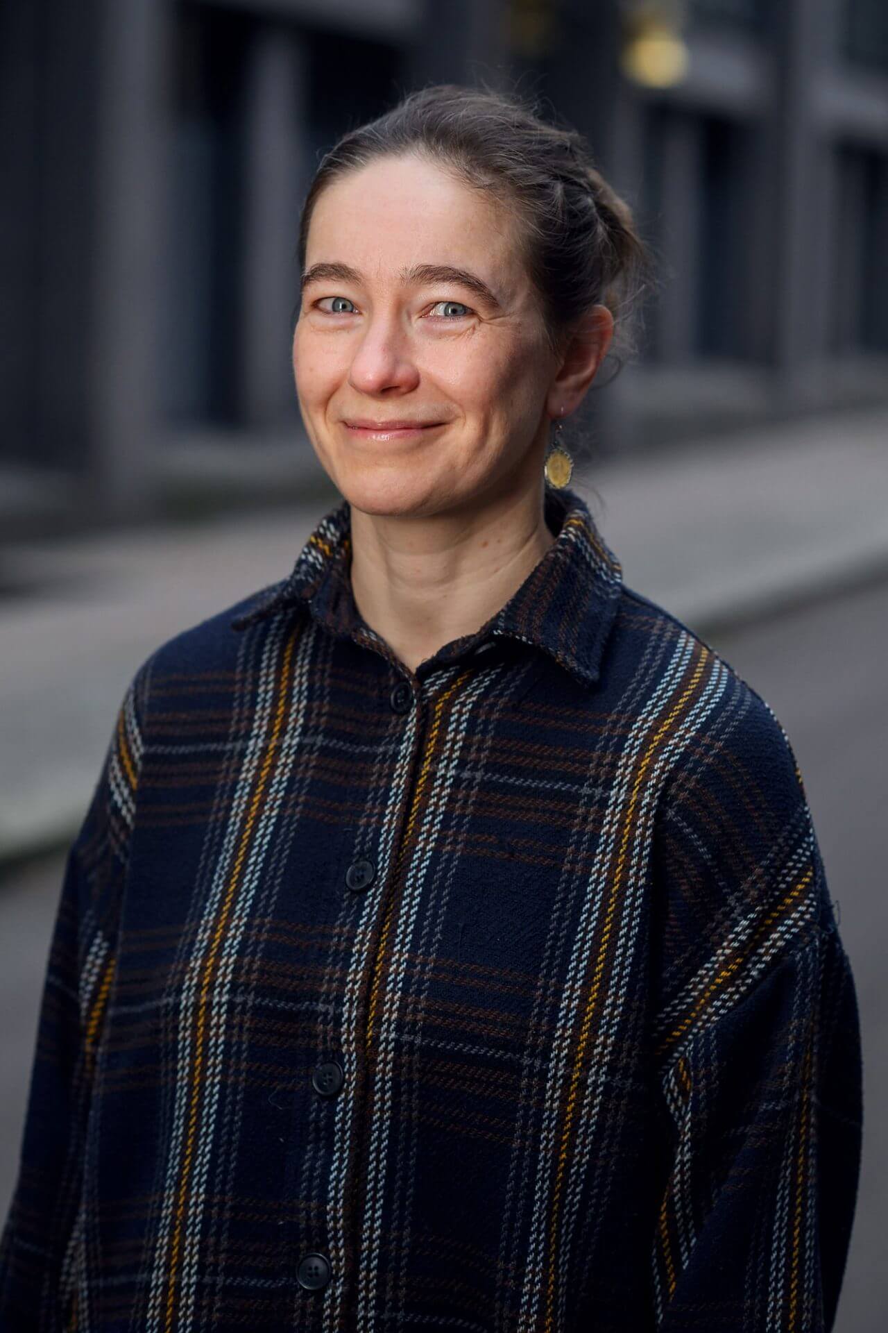 Kvinne med mørkt, oppsatt hår og mørkeblå rutete skjorte.