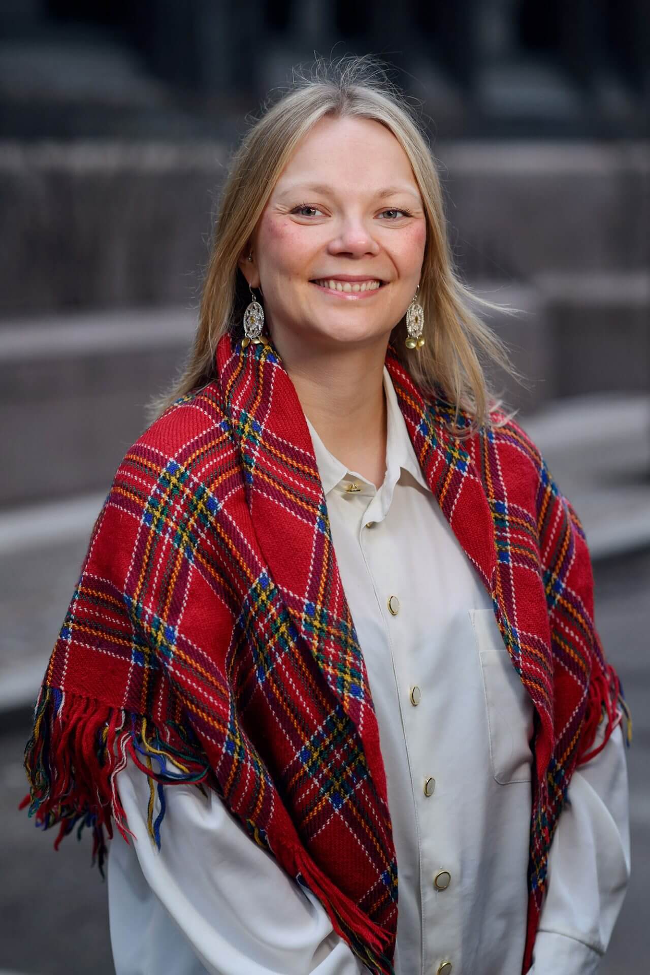 Smilende kvinne med blondt halvlangt hår og rødrutete, samisk sjal rundt skuldrene.