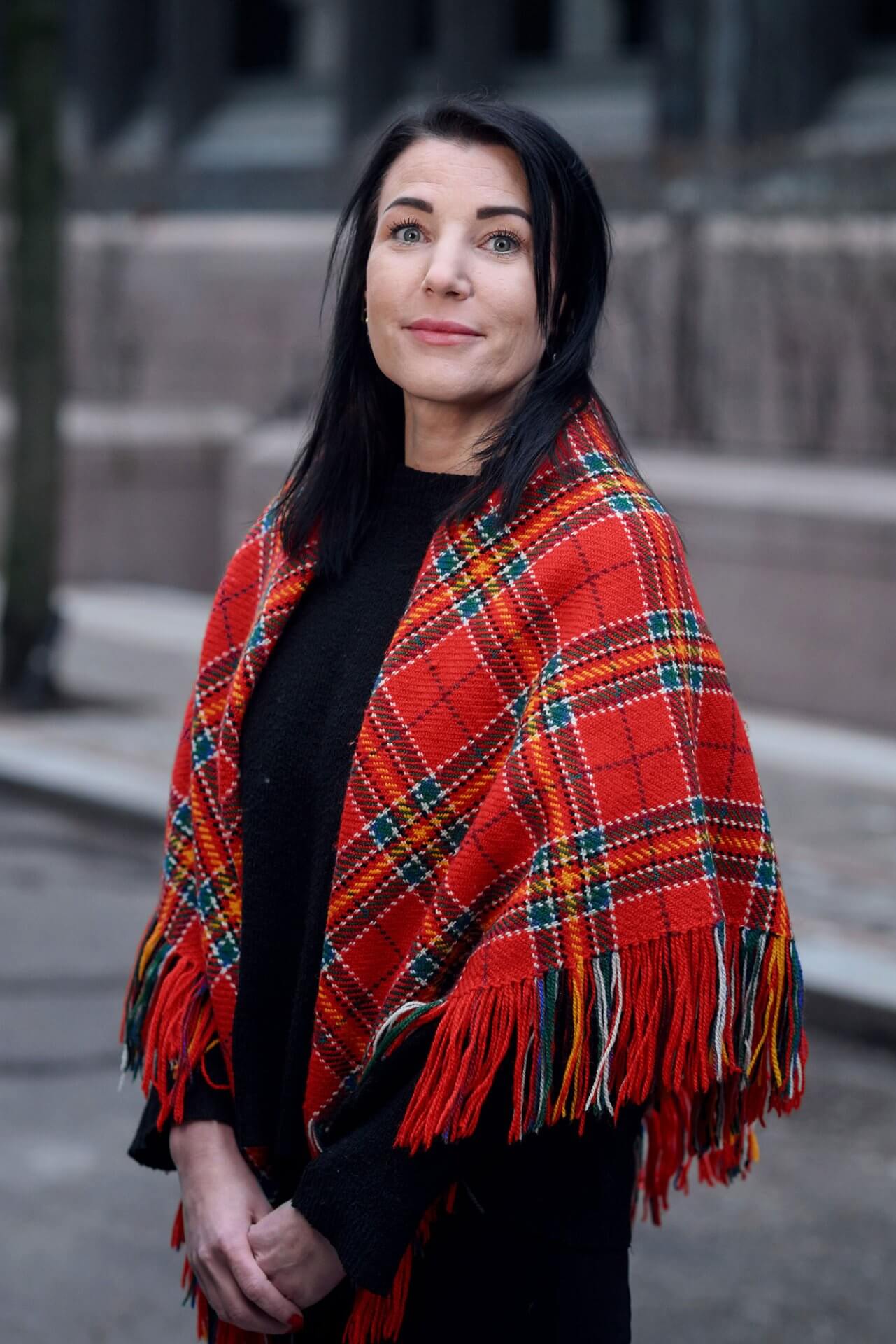 Kvinne med mørkt langt hår, sorte klær og rødrutete, samisk sjal rundt skuldrene.